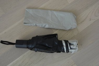 Günlük nesneler. Siyah astarlı açık gri bej şemsiye bej ahşap zeminde duruyor..