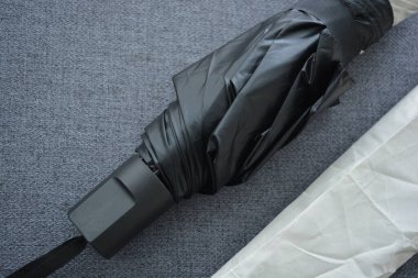 Eşyalar sürekli kullanım nesneleridir. Güzel bir bej, gri şemsiye, siyah astarlı ve kapağı gri kumaş arka planda..