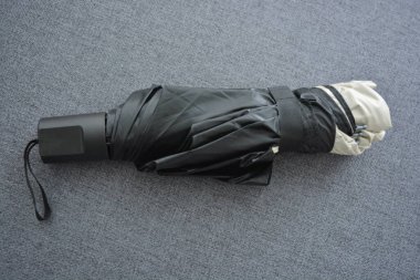 Eşyalar sürekli kullanım nesneleridir. Güzel bir bej, gri şemsiye, siyah astarlı ve kapağı gri kumaş arka planda..