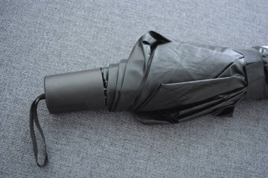 Eşyalar sürekli kullanım nesneleridir. Güzel bir bej, gri şemsiye, siyah astarlı ve kapağı gri kumaş arka planda..