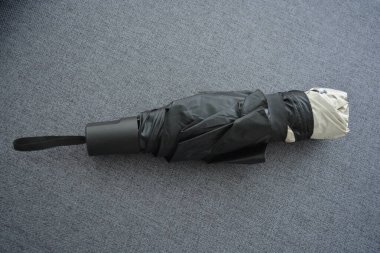 Eşyalar sürekli kullanım nesneleridir. Güzel bir bej, gri şemsiye, siyah astarlı ve kapağı gri kumaş arka planda..