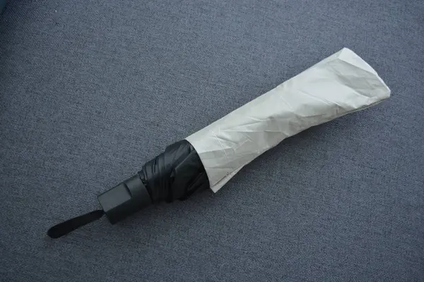 Eşyalar sürekli kullanım nesneleridir. Güzel bir bej, gri şemsiye, siyah astarlı ve kapağı gri kumaş arka planda..