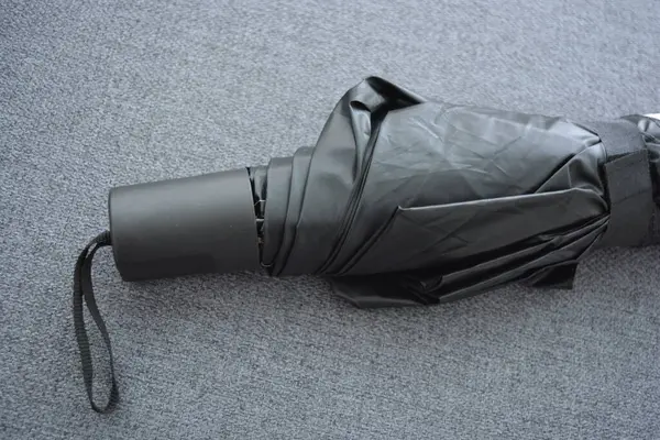 Eşyalar sürekli kullanım nesneleridir. Güzel bir bej, gri şemsiye, siyah astarlı ve kapağı gri kumaş arka planda..