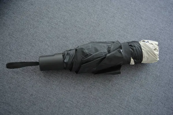 Eşyalar sürekli kullanım nesneleridir. Güzel bir bej, gri şemsiye, siyah astarlı ve kapağı gri kumaş arka planda..