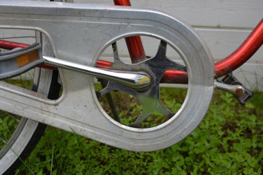 Eşyalar, eşyalar, spor, sağlık. Eski bir kırmızı metal bisiklet yeşil bir çimenlikte beyaz bir çite karşı duruyor. Bisiklet parçaları eski, bisiklet tekerlekleri paslı, bisikletin metal kısımlarında birçok kırmızı pas lekesi var..