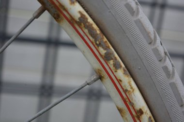 Eşyalar, eşyalar, spor, sağlık. Eski bir kırmızı metal bisiklet yeşil bir çimenlikte beyaz bir çite karşı duruyor. Bisiklet parçaları eski, bisiklet tekerlekleri paslı, bisikletin metal kısımlarında birçok kırmızı pas lekesi var..