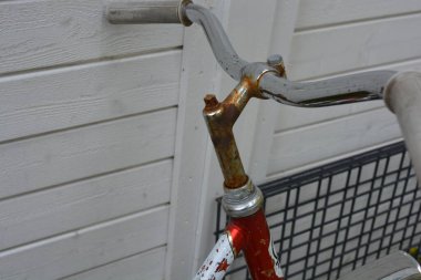 Eşyalar, eşyalar, spor, sağlık. Eski bir kırmızı metal bisiklet yeşil bir çimenlikte beyaz bir çite karşı duruyor. Bisiklet parçaları eski, bisiklet tekerlekleri paslı, bisikletin metal kısımlarında birçok kırmızı pas lekesi var..