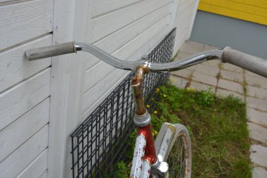 Eşyalar, eşyalar, spor, sağlık. Eski bir kırmızı metal bisiklet yeşil bir çimenlikte beyaz bir çite karşı duruyor. Bisiklet parçaları eski, bisiklet tekerlekleri paslı, bisikletin metal kısımlarında birçok kırmızı pas lekesi var..