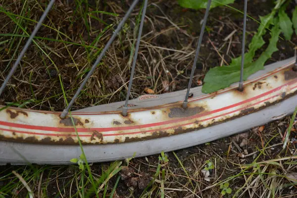 Eşyalar, eşyalar, spor, sağlık. Eski bir kırmızı metal bisiklet yeşil bir çimenlikte beyaz bir çite karşı duruyor. Bisiklet parçaları eski, bisiklet tekerlekleri paslı, bisikletin metal kısımlarında birçok kırmızı pas lekesi var..