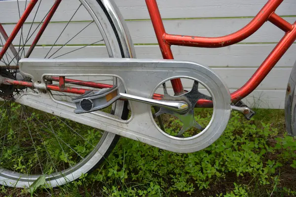 Eşyalar, eşyalar, spor, sağlık. Eski bir kırmızı metal bisiklet yeşil bir çimenlikte beyaz bir çite karşı duruyor. Bisiklet parçaları eski, bisiklet tekerlekleri paslı, bisikletin metal kısımlarında birçok kırmızı pas lekesi var..
