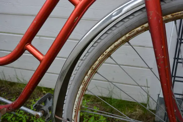 Eşyalar, eşyalar, spor, sağlık. Eski bir kırmızı metal bisiklet yeşil bir çimenlikte beyaz bir çite karşı duruyor. Bisiklet parçaları eski, bisiklet tekerlekleri paslı, bisikletin metal kısımlarında birçok kırmızı pas lekesi var..