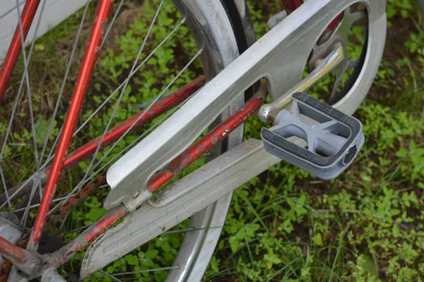 Eşyalar, eşyalar, spor, sağlık. Eski bir kırmızı metal bisiklet yeşil bir çimenlikte beyaz bir çite karşı duruyor. Bisiklet parçaları eski, bisiklet tekerlekleri paslı, bisikletin metal kısımlarında birçok kırmızı pas lekesi var..