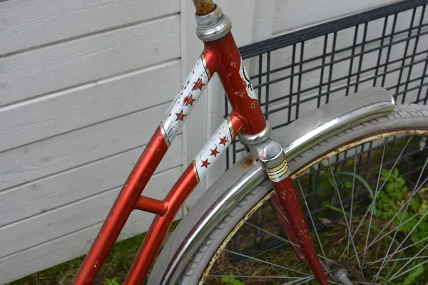 Eşyalar, eşyalar, spor, sağlık. Eski bir kırmızı metal bisiklet yeşil bir çimenlikte beyaz bir çite karşı duruyor. Bisiklet parçaları eski, bisiklet tekerlekleri paslı, bisikletin metal kısımlarında birçok kırmızı pas lekesi var..