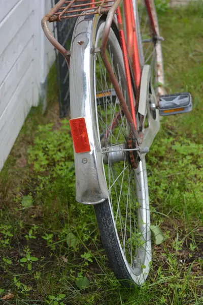 Eşyalar, eşyalar, spor, sağlık. Eski bir kırmızı metal bisiklet yeşil bir çimenlikte beyaz bir çite karşı duruyor. Bisiklet parçaları eski, bisiklet tekerlekleri paslı, bisikletin metal kısımlarında birçok kırmızı pas lekesi var..