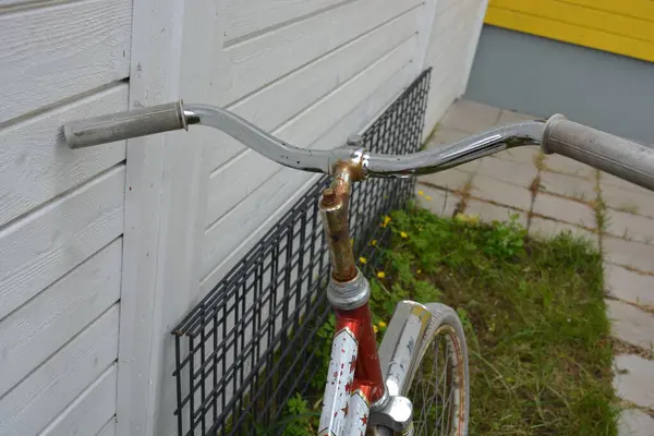 Eşyalar, eşyalar, spor, sağlık. Eski bir kırmızı metal bisiklet yeşil bir çimenlikte beyaz bir çite karşı duruyor. Bisiklet parçaları eski, bisiklet tekerlekleri paslı, bisikletin metal kısımlarında birçok kırmızı pas lekesi var..