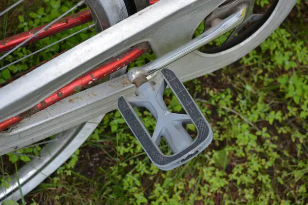 Eşyalar, eşyalar, spor, sağlık. Eski bir kırmızı metal bisiklet yeşil bir çimenlikte beyaz bir çite karşı duruyor. Bisiklet parçaları eski, bisiklet tekerlekleri paslı, bisikletin metal kısımlarında birçok kırmızı pas lekesi var..