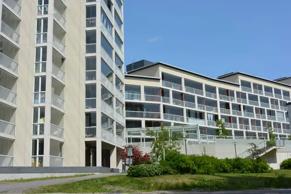 Apartments, houses, real estate located by the sea bay and illuminated by the rays of the sun in Espoo city, Finland. New white houses with large glass balconies are located among tall green trees, firs, pines.
