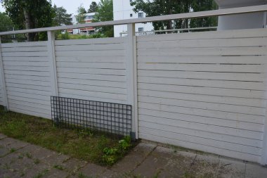 Bina, inşaat, bina. Doğal çam ağacından yapılmış beyaz ahşap çit ve yeşil bir alana sahip beyaz boyayla kaplanmış çimen, beton yollar..