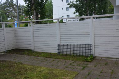 Bina, inşaat, bina. Doğal çam ağacından yapılmış beyaz ahşap çit ve yeşil bir alana sahip beyaz boyayla kaplanmış çimen, beton yollar..