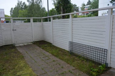 Bina, inşaat, bina. Doğal çam ağacından yapılmış beyaz ahşap çit ve yeşil bir alana sahip beyaz boyayla kaplanmış çimen, beton yollar..