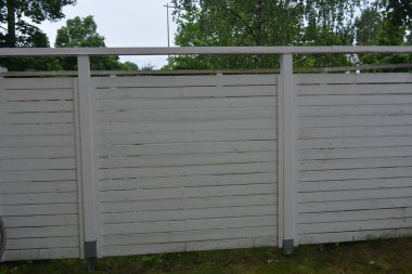 Bina, inşaat, bina. Doğal çam ağacından yapılmış beyaz ahşap çit ve yeşil bir alana sahip beyaz boyayla kaplanmış çimen, beton yollar..