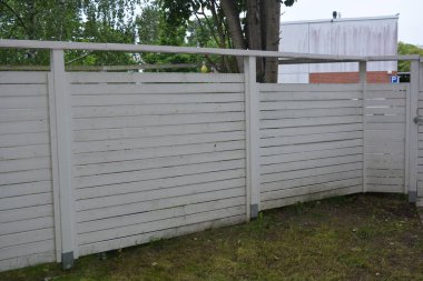 Bina, inşaat, bina. Doğal çam ağacından yapılmış beyaz ahşap çit ve yeşil bir alana sahip beyaz boyayla kaplanmış çimen, beton yollar..