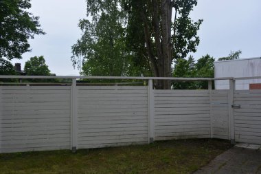 Bina, inşaat, bina. Doğal çam ağacından yapılmış beyaz ahşap çit ve yeşil bir alana sahip beyaz boyayla kaplanmış çimen, beton yollar..