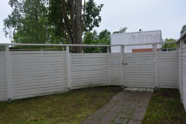 Bina, inşaat, bina. Doğal çam ağacından yapılmış beyaz ahşap çit ve yeşil bir alana sahip beyaz boyayla kaplanmış çimen, beton yollar..