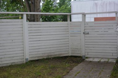 Bina, inşaat, bina. Doğal çam ağacından yapılmış beyaz ahşap çit ve yeşil bir alana sahip beyaz boyayla kaplanmış çimen, beton yollar..