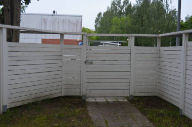 Bina, inşaat, bina. Doğal çam ağacından yapılmış beyaz ahşap çit ve yeşil bir alana sahip beyaz boyayla kaplanmış çimen, beton yollar..