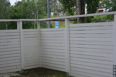 Bina, inşaat, bina. Doğal çam ağacından yapılmış beyaz ahşap çit ve yeşil bir alana sahip beyaz boyayla kaplanmış çimen, beton yollar..