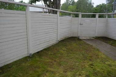 Bina, inşaat, bina. Doğal çam ağacından yapılmış beyaz ahşap çit ve yeşil bir alana sahip beyaz boyayla kaplanmış çimen, beton yollar..