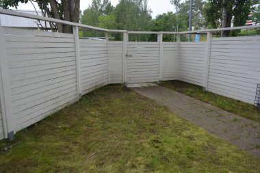 Bina, inşaat, bina. Doğal çam ağacından yapılmış beyaz ahşap çit ve yeşil bir alana sahip beyaz boyayla kaplanmış çimen, beton yollar..