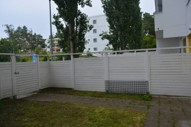 Bina, inşaat, bina. Doğal çam ağacından yapılmış beyaz ahşap çit ve yeşil bir alana sahip beyaz boyayla kaplanmış çimen, beton yollar..