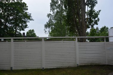 Bina, inşaat, bina. Doğal çam ağacından yapılmış beyaz ahşap çit ve yeşil bir alana sahip beyaz boyayla kaplanmış çimen, beton yollar..