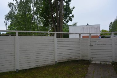 Bina, inşaat, bina. Doğal çam ağacından yapılmış beyaz ahşap çit ve yeşil bir alana sahip beyaz boyayla kaplanmış çimen, beton yollar..