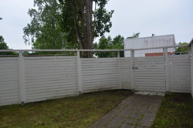 Bina, inşaat, bina. Doğal çam ağacından yapılmış beyaz ahşap çit ve yeşil bir alana sahip beyaz boyayla kaplanmış çimen, beton yollar..