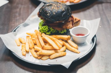 Biftek olarak patates kızartmalı kızarmış tavukla doldurulmuş kömürlü hamburgerin yakın çekimi. Restoranda tavuk burger..