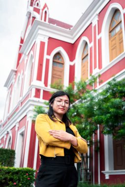 Beautiful asian woman (LGBTQ) natural makeup wear fashion yellow leather clothes with glasses posing at old town and vintage building outdoor fashion style clipart