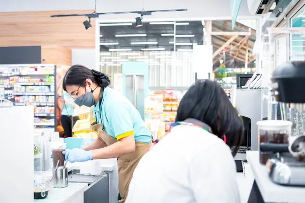 Asyalı kadın, kahve dükkanındaki müşterilere kahve servisi için sütlü kahve fincanına kahve yapmak için kahve köpüğü döken bir barista olarak çalışıyor.