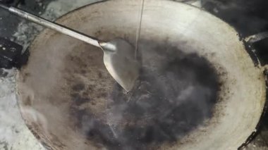 Asyalı aşçı Tayland mutfağında geleneksel kırsal kesimde yemek pişiriyor. Geleneksel bir tavaya dökülen akarsu bitkisel yağları, yüksek sıcaklıkta pişirme, kızartma ve yiyecek hazırlıyor.