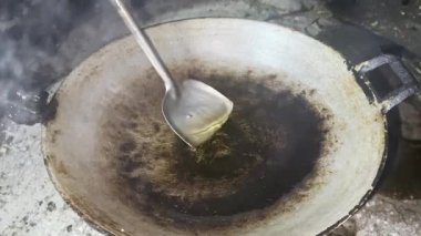 Asyalı aşçı Tayland mutfağında geleneksel kırsal kesimde yemek pişiriyor. Geleneksel bir tavaya dökülen akarsu bitkisel yağları, yüksek sıcaklıkta pişirme, kızartma ve yiyecek hazırlıyor.