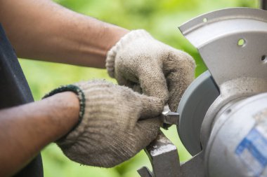 İşçi makyaj tekeriyle torna takımını yeniden öğütüyor. Makine operatörü tarafından kesme araçları yeniden öğütme işlemi.