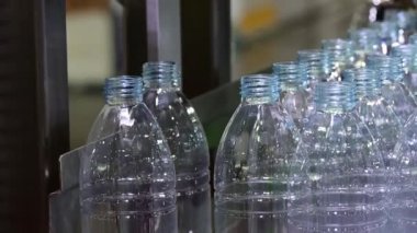 Su fabrikasındaki işlemleri tamamlamak için taşıma bandındaki korkuluktaki evcil hayvan şişeleri. Fabrikadaki otomatik doldurma makinesinin içme suyu üretim süreci.. 