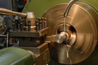 Torna makinesi metal şaft parçalarını sıvı soğutucu metoduyla kesiyor. Torna makinesi operatörü soğutucu tüpünü elle kuruyor..