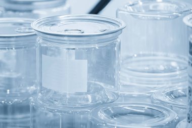 Açık mavi sahnede alüminyum kapaklı şeffaf plastik kap. Plastik konteynır üretim süreci.