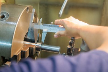 Sahneyi kapat. Dönüş makinası operatörü, metal şaft parçalarını Vernier Caliper 'a göre ölçüyor. Dönüş makinesinin kalite kontrolü. 