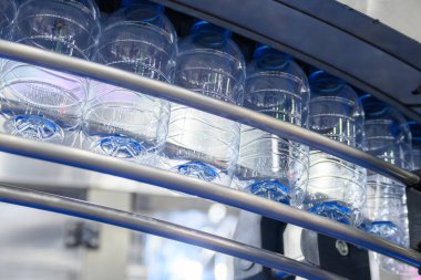 İçme suyu şişeleri doldurmak için taşıyıcı bantta asılı. İçme suyu üretim sürecinin yüksek teknolojisi. 