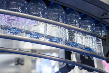 İçme suyu şişeleri doldurmak için taşıyıcı bantta asılı. İçme suyu üretim sürecinin yüksek teknolojisi. 