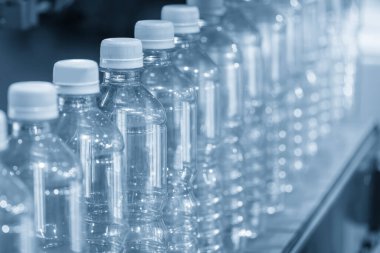 Açık mavi sahnede içme suyu üretim sürecinin yüksek teknolojisi. Taşıma bandındaki boş içme suyu şişelerini doldurmak için.. 